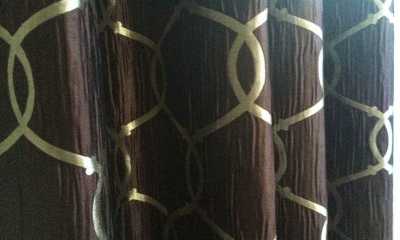 Dark brown patterned, blackout grommet style draperies up close.